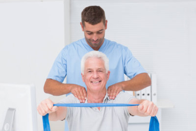 Male physiotherapist assisting senior patient in exercising with resistance band at clinic
