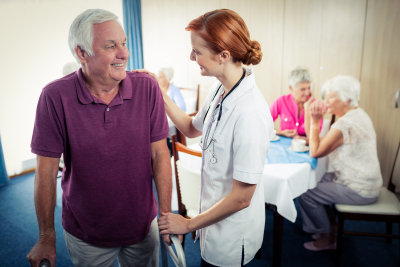 nurse assisting an elder man in using a walker