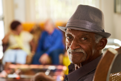 elderly man looking in retirement home, with group of friends in background