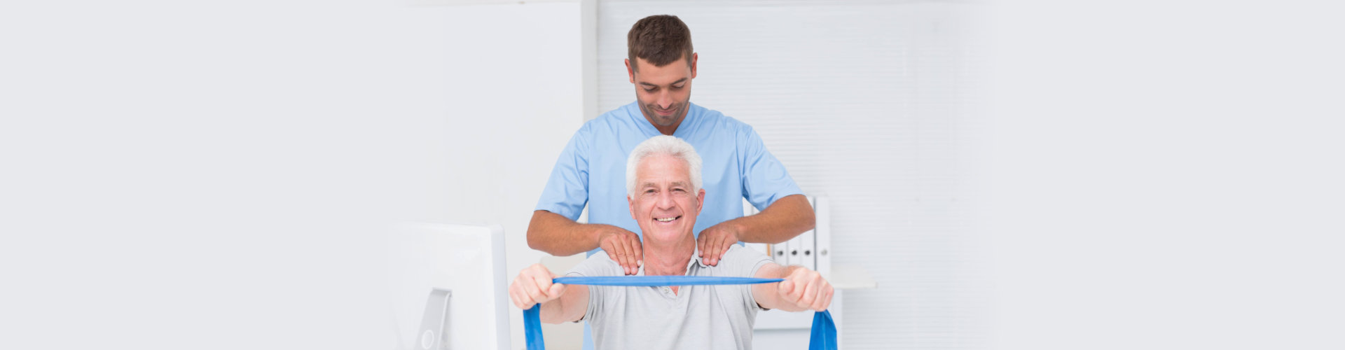 Male physiotherapist assisting senior patient in exercising with resistance band at clinic